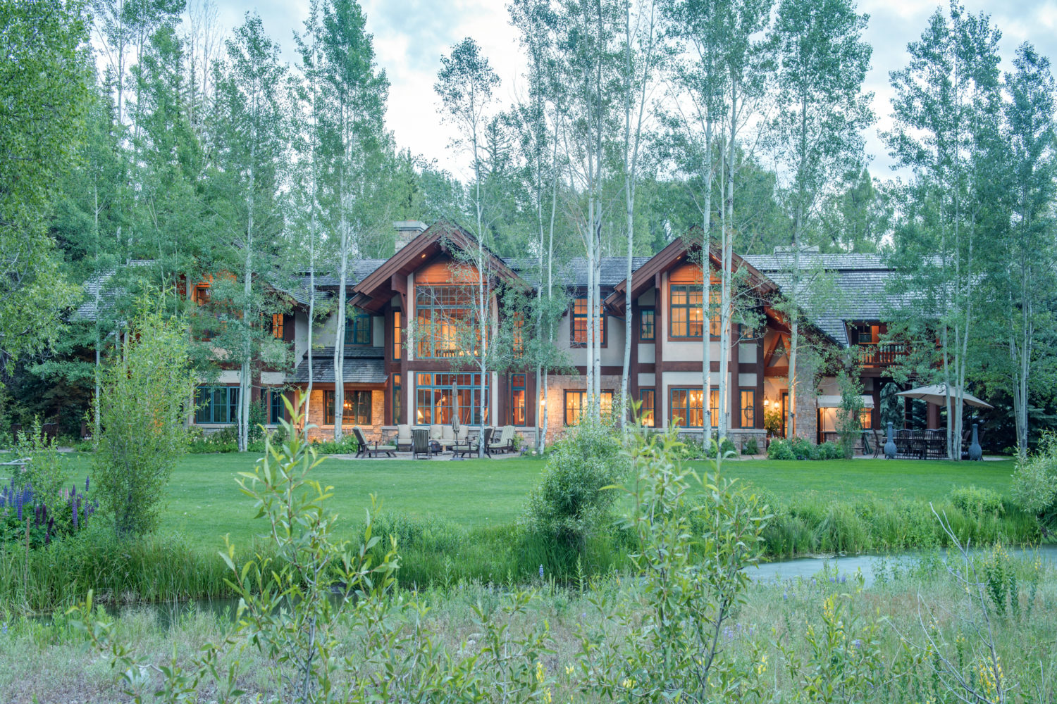 A creek and lawn in front of a big house surrounded by aspens