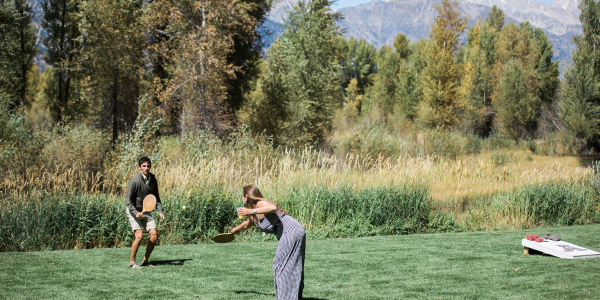 A couple plays paddleball on the lawn in front of the mountains