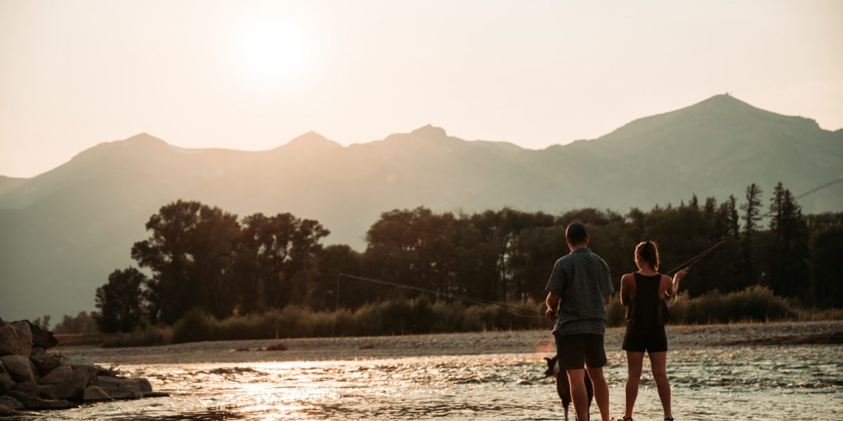 A man and woman fly fish on the river during sunset