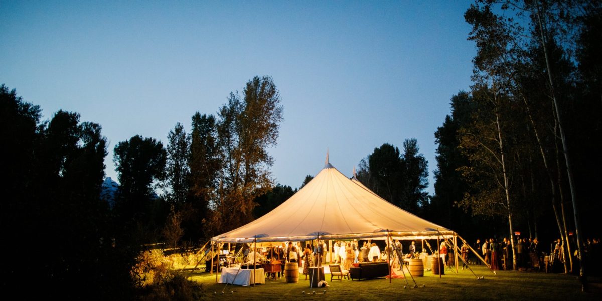 A large tent full of guests is lit up at night while surrounded by trees
