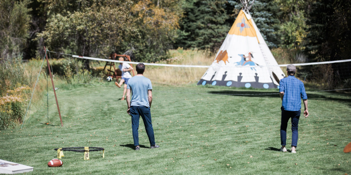 A group of friends play lawn games in front of a teepee