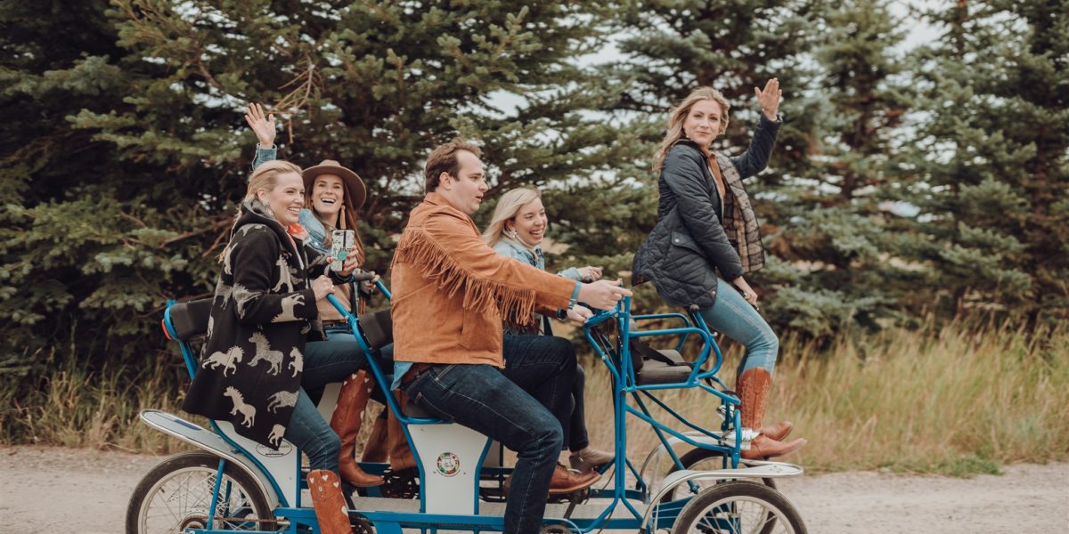 A group of friends smile while riding a multi-person bike