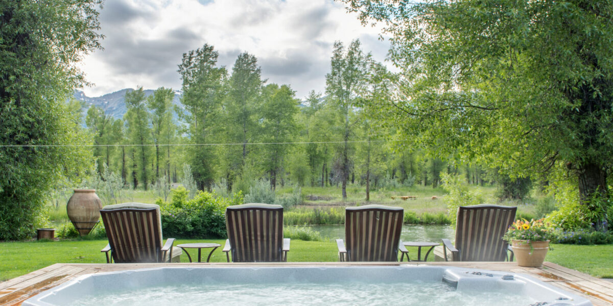 A large hot tub and lawn chairs in front of trees and mountains