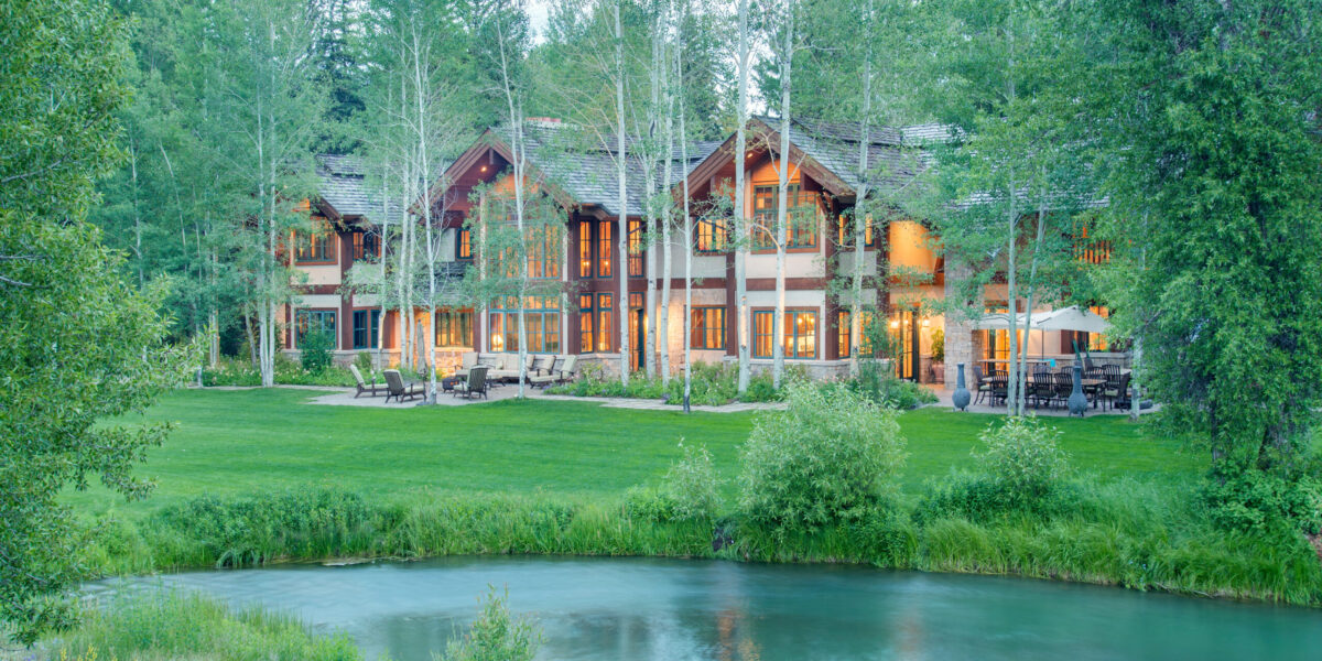 A large home surrounded by trees in front of a creek