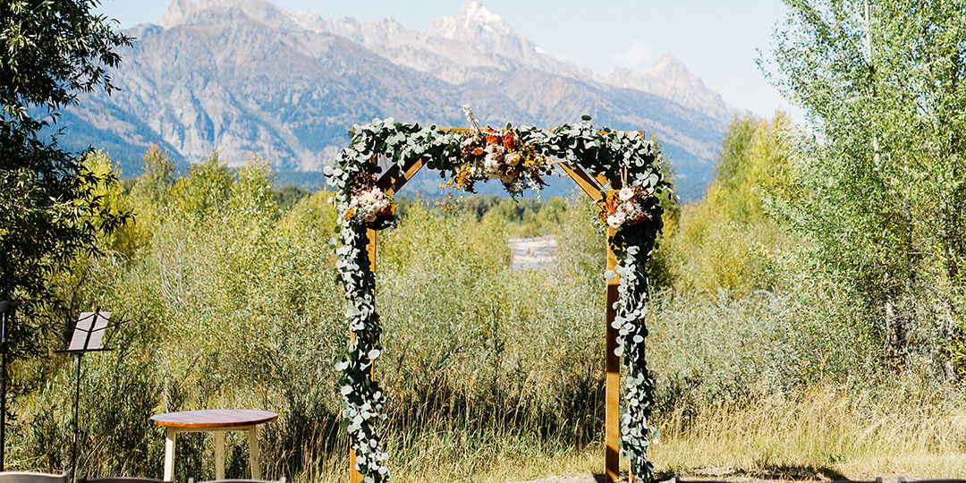 A flower arch wedding altar in front of empty chairs and with mountains behind it