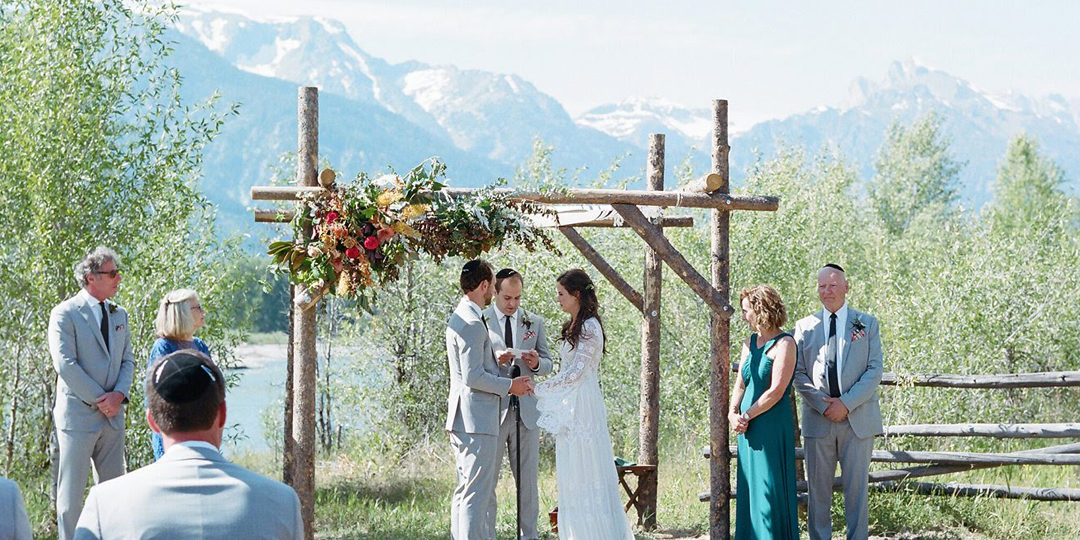 A bride and groom getting married under a chuppah in front of mountains